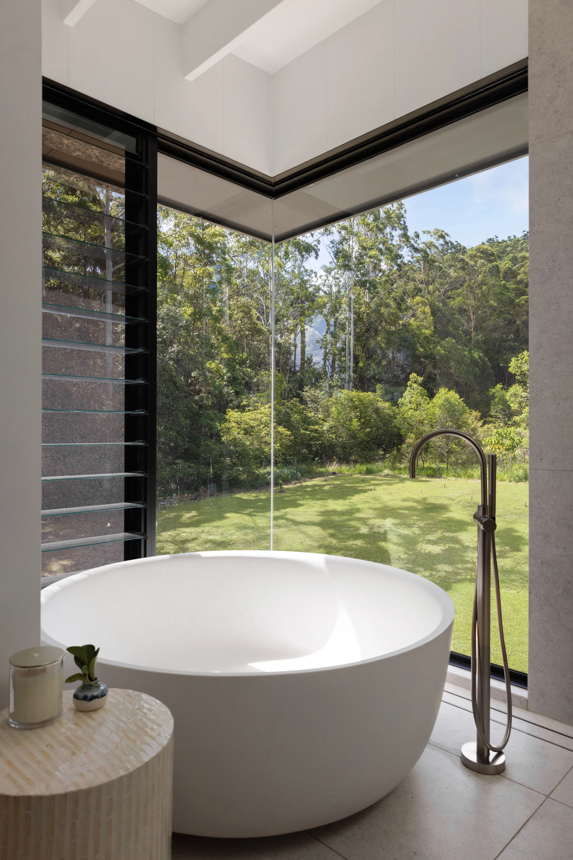 Freestanding bath beside corner glazing overlooking the trees