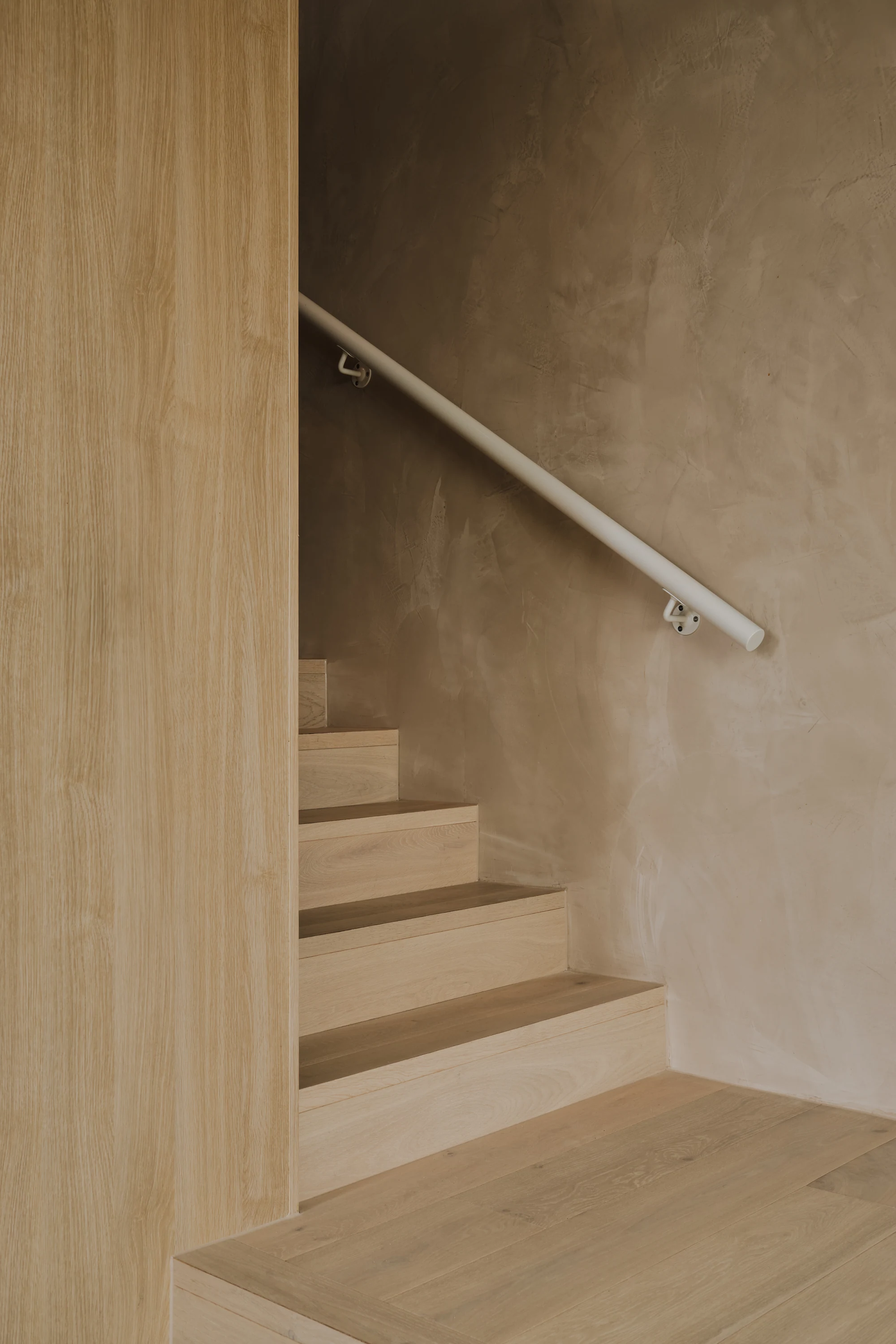Timber stair with a slender handrail and textured wall at Palmera