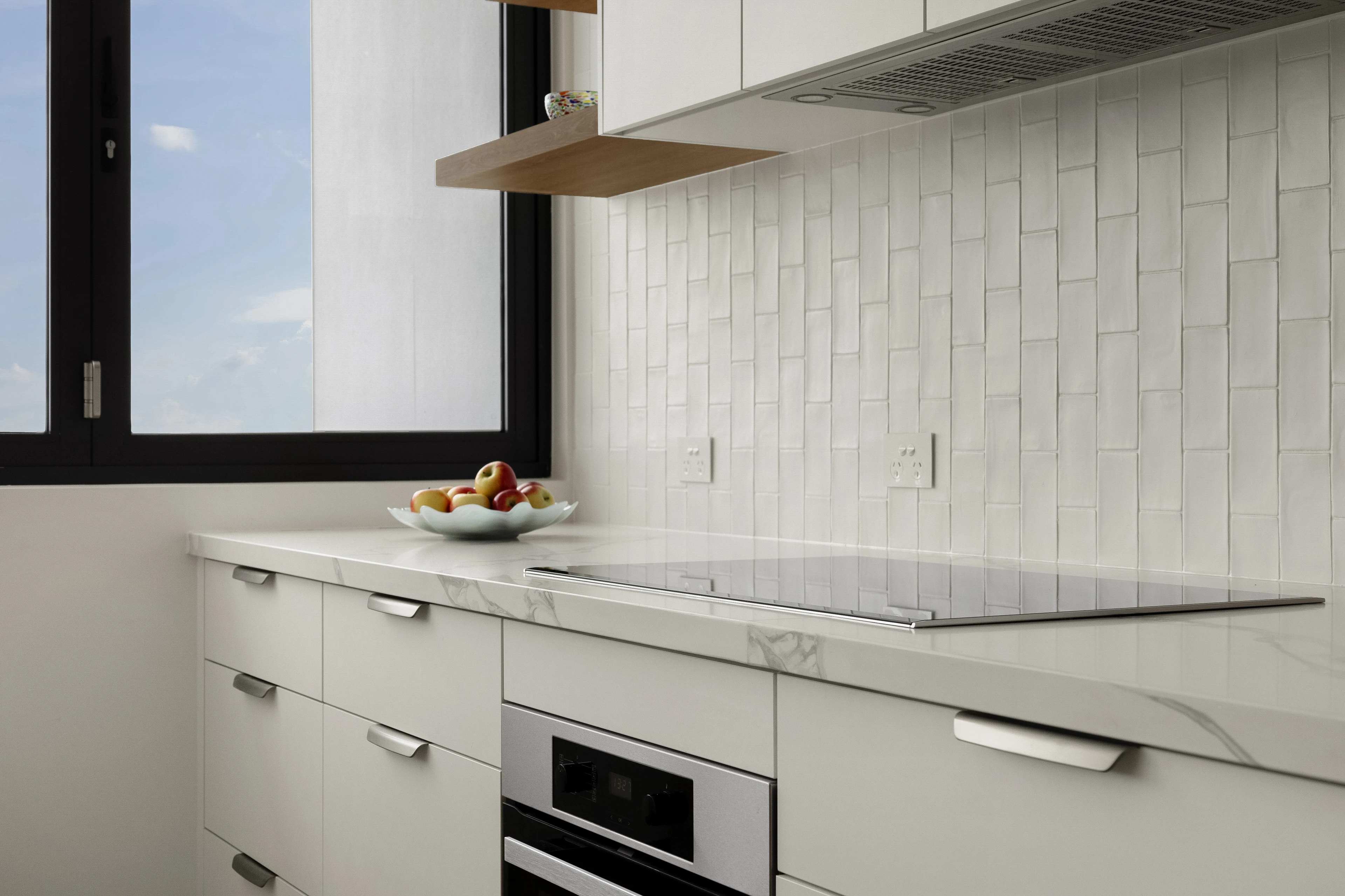 Pale kitchen cabinetry, stone benchtop and tiled splashback