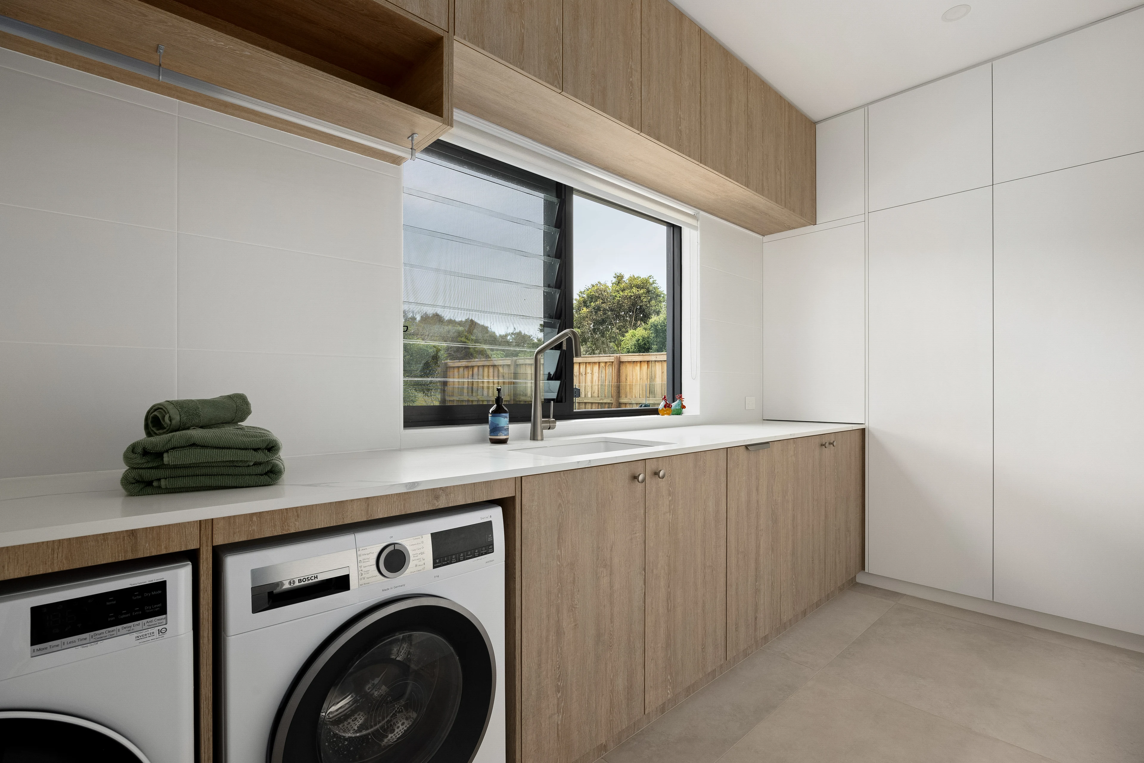 Timber laundry joinery and a long stone benchtop beneath the window