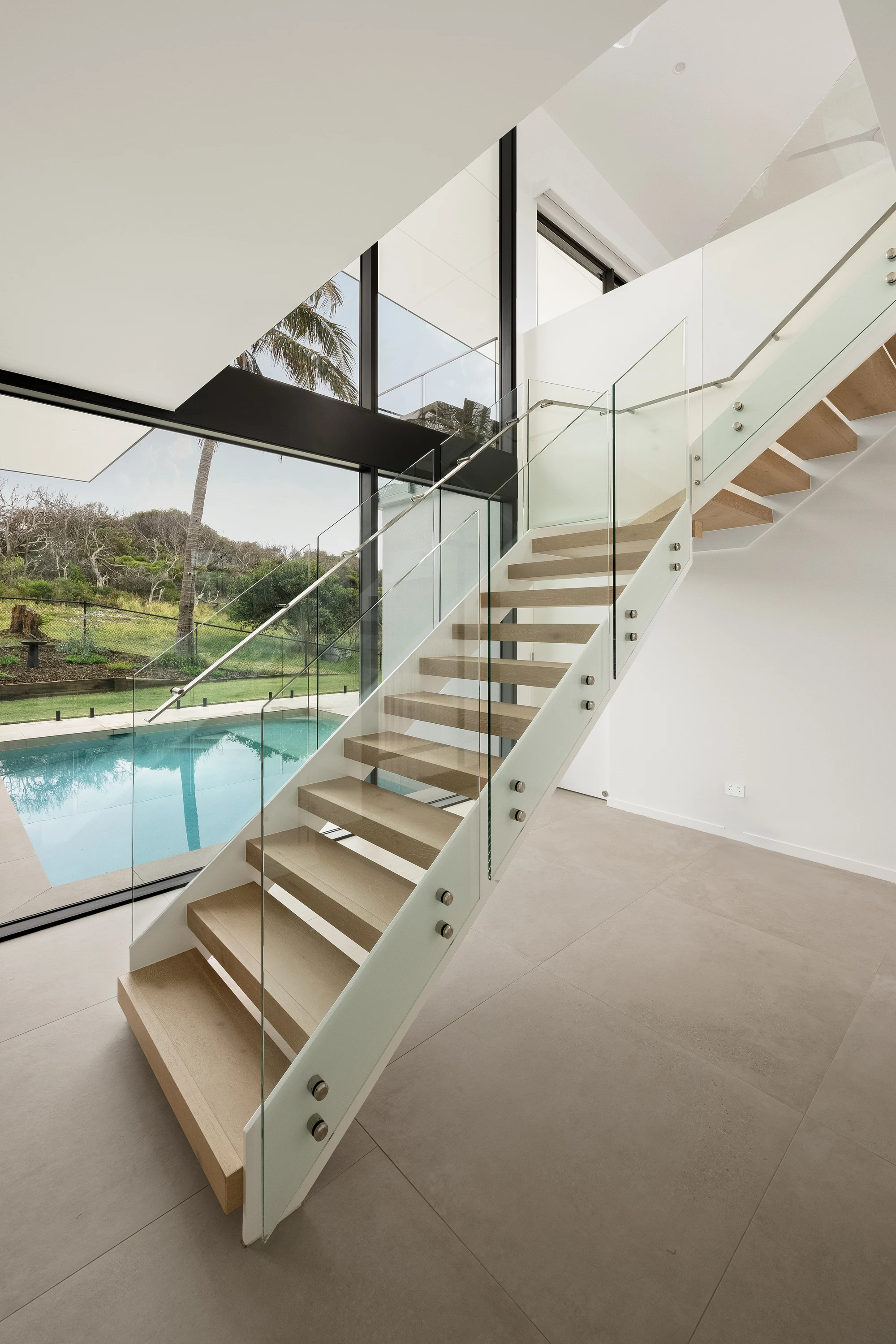 Timber staircase and double-height glazing overlooking the pool at 47 Wavecrest