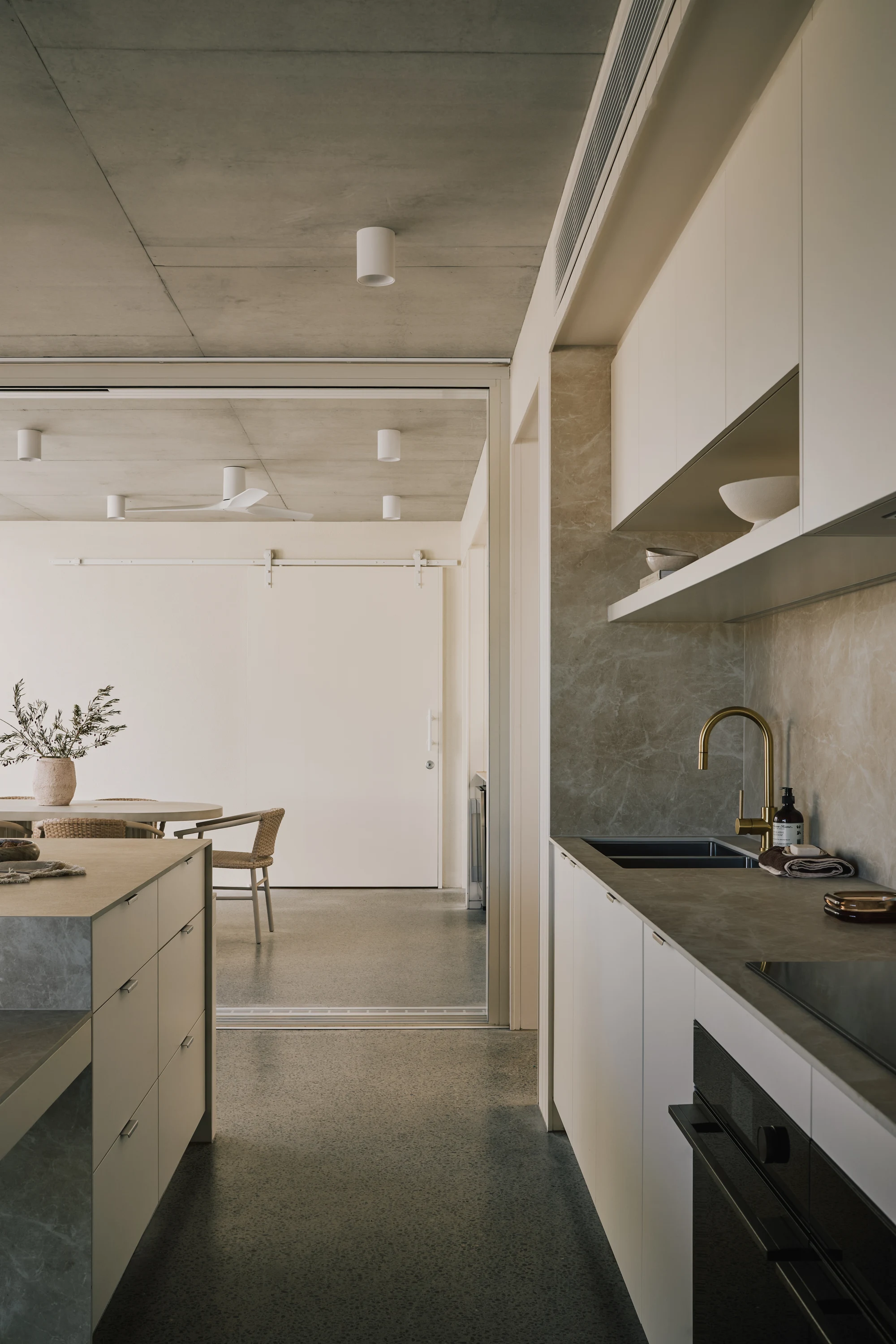 Stone kitchen and timber joinery beneath an exposed concrete ceiling